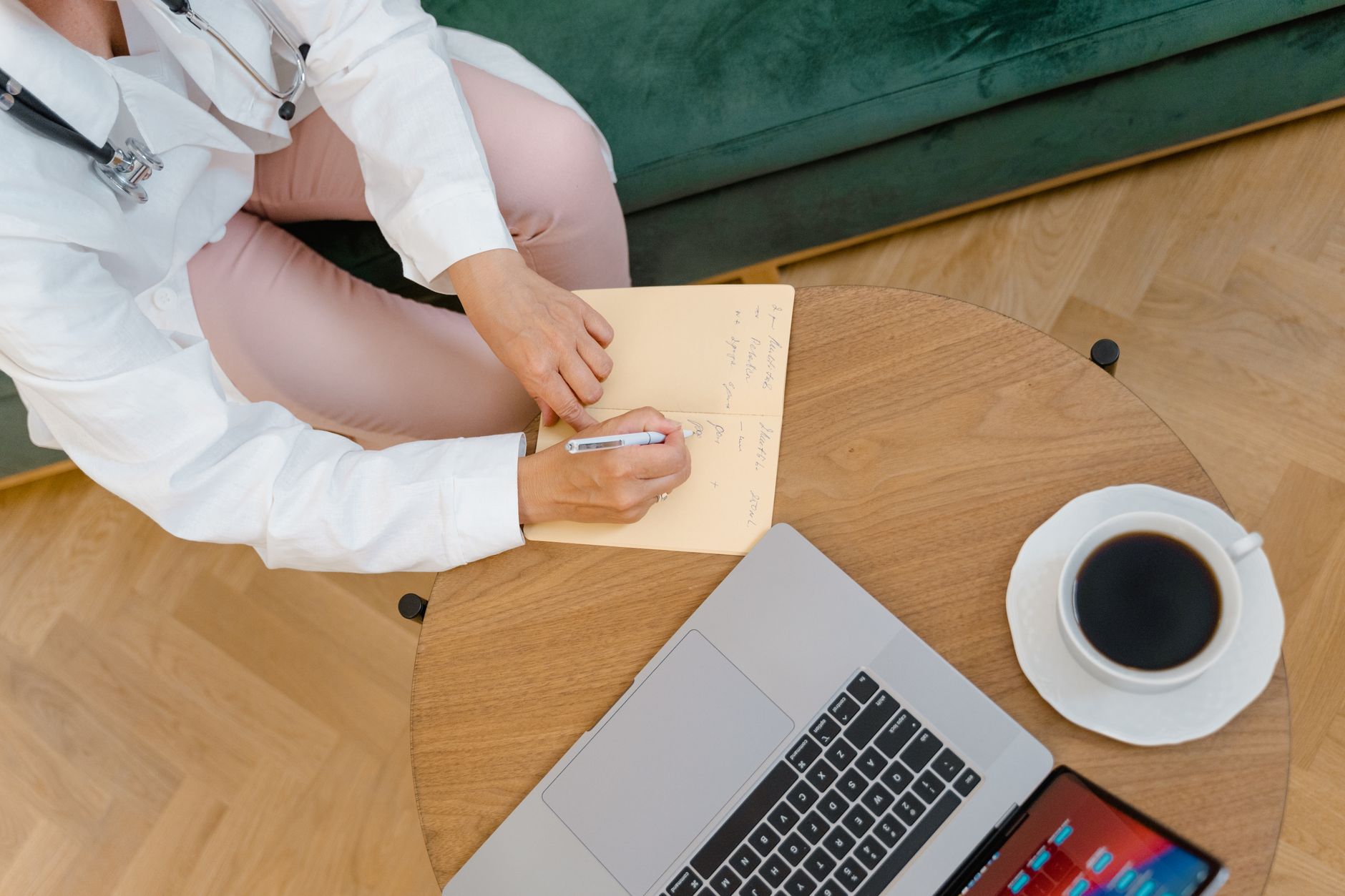 Vista de cima de uma mesa de consultório com anotações à mão, um laptop e um café