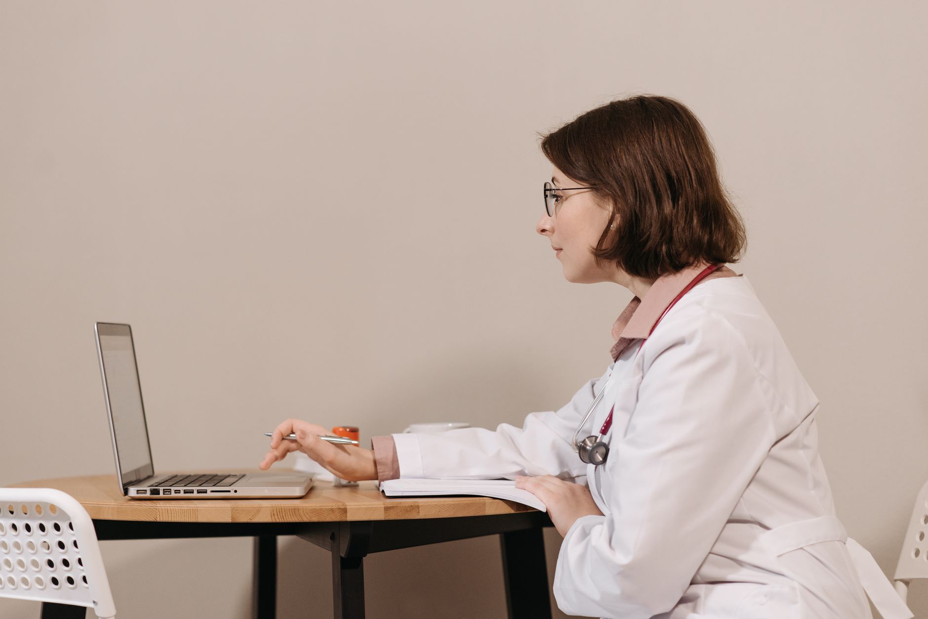 Profissional de saúde de jaleco branco durante uma consulta por vídeo, no consultório